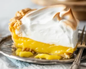Slice of homemade lemon meringue pie with fluffy meringue topping and flaky crust.