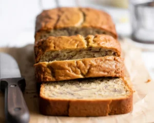 Slice of moist banana bread made with buttermilk on a wooden cutting board.