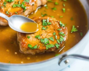 Juicy pork chops served with a rich sauce in a skillet.