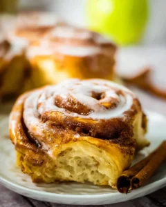 Freshly baked apple cinnamon rolls topped with icing on a rustic wooden table.
