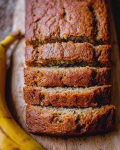 Slice of moist banana bread on a wooden cutting board