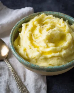 A bowl of creamy mashed potatoes topped with butter and herbs
