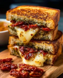 Delicious sun-dried tomato bacon pesto grilled cheese sandwich on a plate.